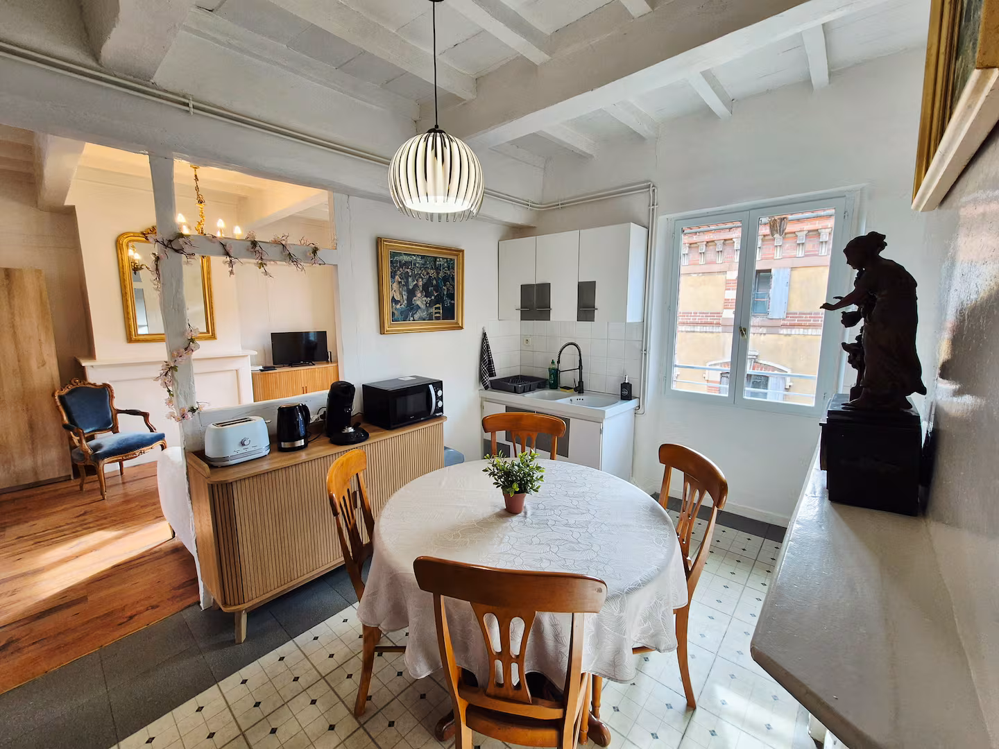 La cuisine du logement : table ronde dressée, façades de brique par la fenêtre